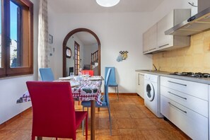 Une cuisine compacte équipée d’un lave-linge, un coin repas avec une table et des chaises, et une grande fenêtre.