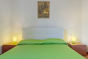 Une chambre à coucher comprenant un lit, deux tables de chevet, une commode, un tableau accroché au mur et une prise électrique.