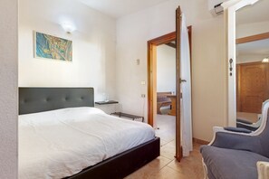 A bedroom with a bed, a chair, a painting on the wall, and a door leading to another room. - Elegant and welcoming 70 square meters townhouse, perfect for six people, with a private entrance and spread over two floors.The property is located in Villasimius, a town known for its splendid sandy beaches and crystal-clear sea. The apartment is centr (Villasimius)