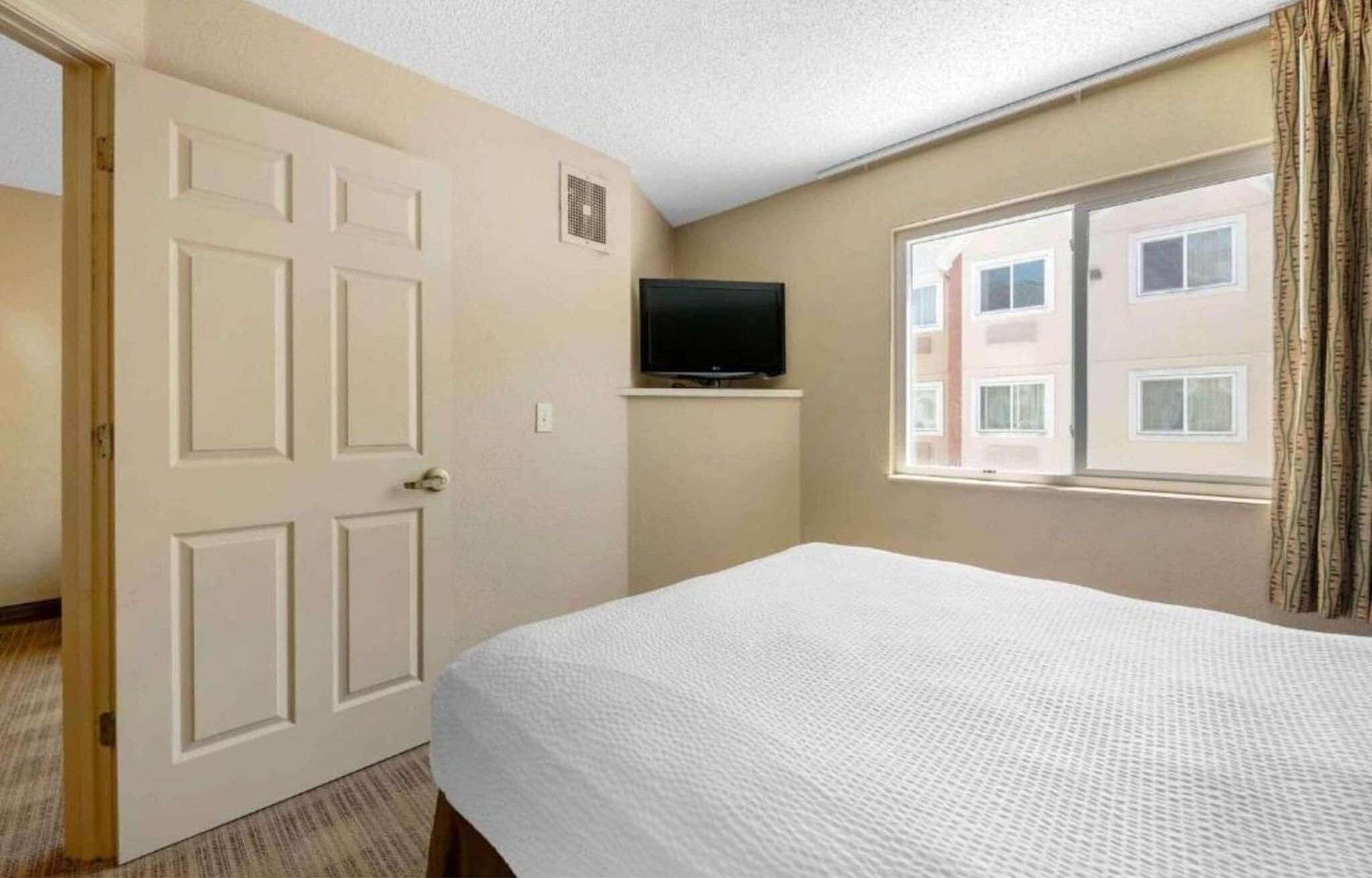 Camera d'albergo con un letto, una televisione su un ripiano, una porta e una finestra vista edifici.