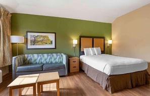 Une chambre d’hôtel avec un lit, un canapé, une petite table, une table de chevet, une lampe et un tableau encadré au mur.