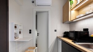 A compact kitchen with a microwave, toaster, and sink. There is a door leading to a small room, and a white cabinet with shelves. - Oraya Chic Studio with Balcony in Athens (Athens)
