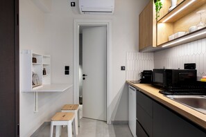 A compact kitchen with a microwave, toaster, and sink. There is a door leading to a small room, and a white cabinet with shelves.
