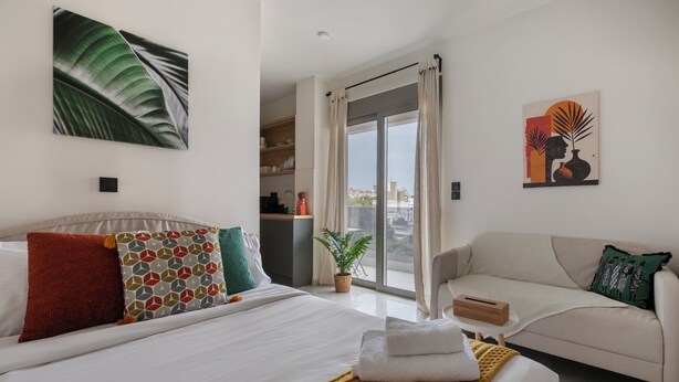 A hotel room with a bed, a sofa, a window with curtains, a plant, and artwork on the walls. - Oraya Chic Studio with Balcony in Athens (Athens)