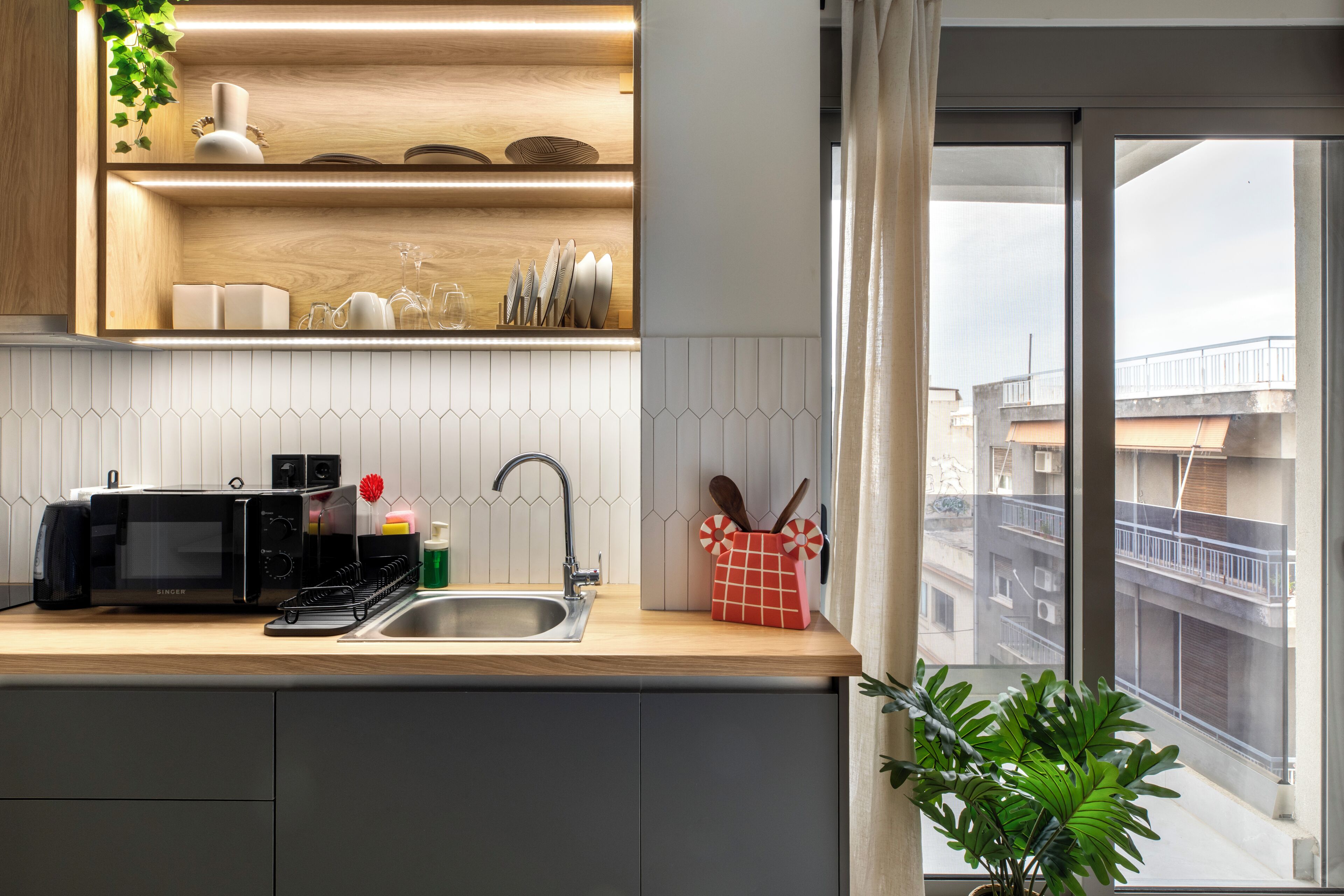 A modern kitchen with a microwave, sink, and wooden shelves.