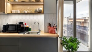 A modern kitchen with a microwave, sink, and wooden shelves. - Oraya Chic Studio with Balcony in Athens (Athens)