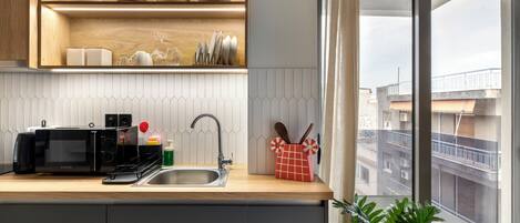 A modern kitchen with a microwave, sink, and wooden shelves.
