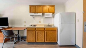 A compact kitchen with wooden cabinets, a white refrigerator, a microwave, a stove, and a dining area with a chair and table. - 1 Full Bed | Smoking, Kitchen (Oklahoma City OK)