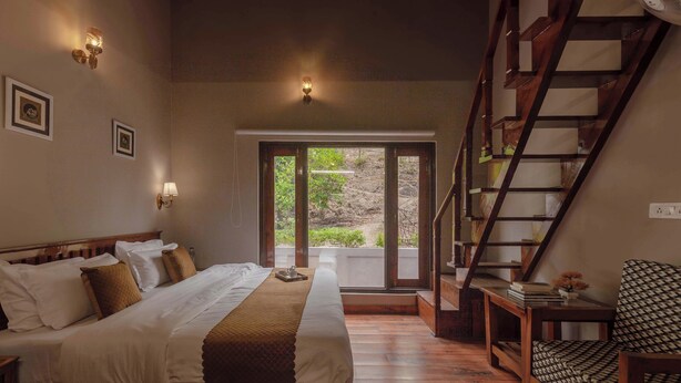A bedroom with a large bed, a wooden staircase, and a view through a glass door. - Alaya Stays Amara Dawn (Naina Range)