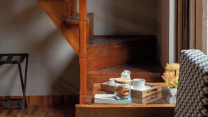 A wooden staircase leading to a landing with a table set with tea and cookies, a chair, and a window with curtains. - Alaya Stays Amara Dawn (Naina Range)