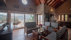 A spacious living area with a high ceiling, wooden beams, a large window with a view, and a dining area with patterned furniture. - Alaya Stays Amara Dawn (Naina Range)