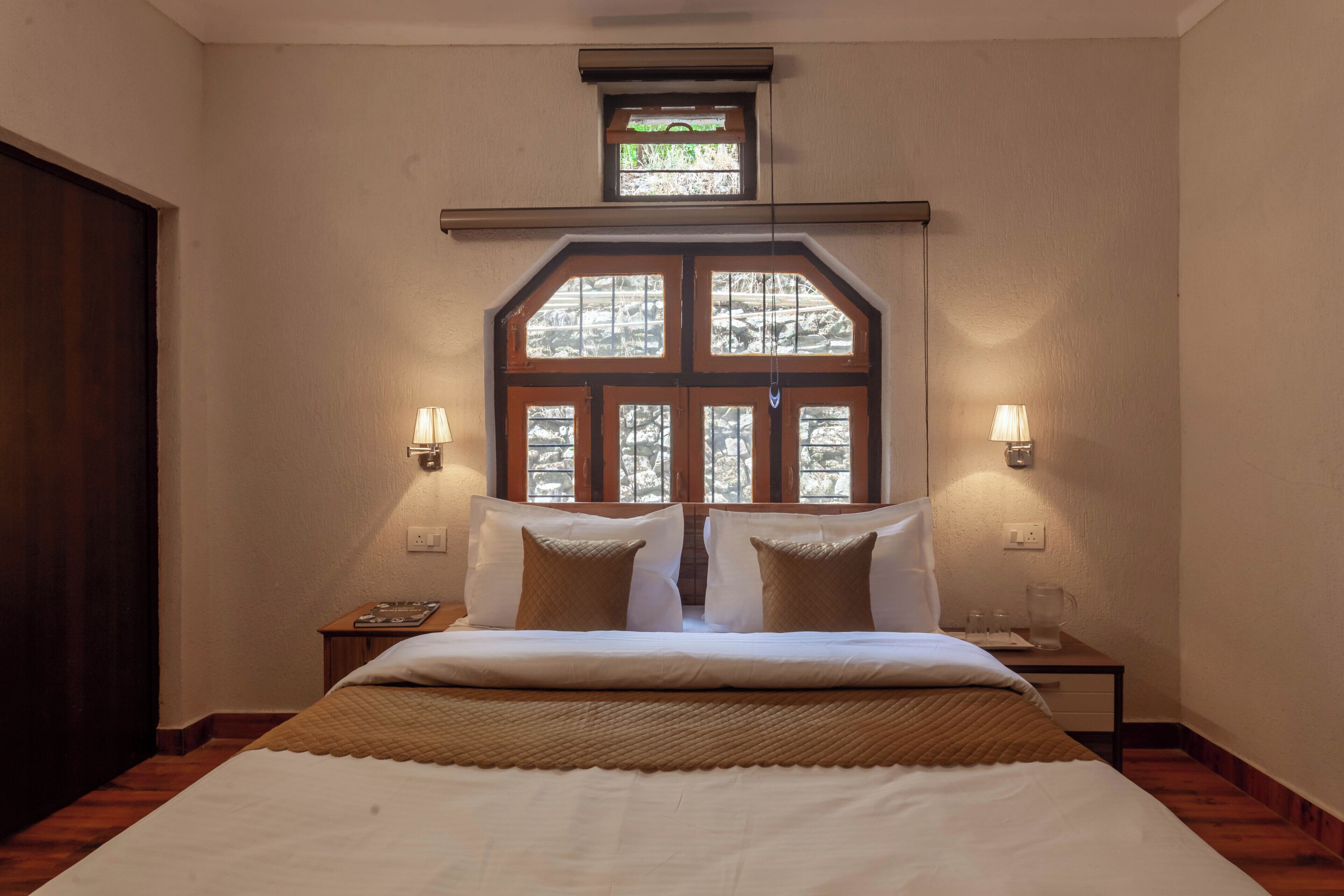 Un dormitorio con una cama grande, dos mesitas de noche, un ventanal con vistas y un tragaluz pequeño sobre el ventanal.