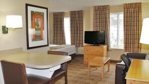 Une chambre d’hôtel comprenant un lit, une télévision, une table à manger avec des chaises et une fenêtre avec des rideaux.