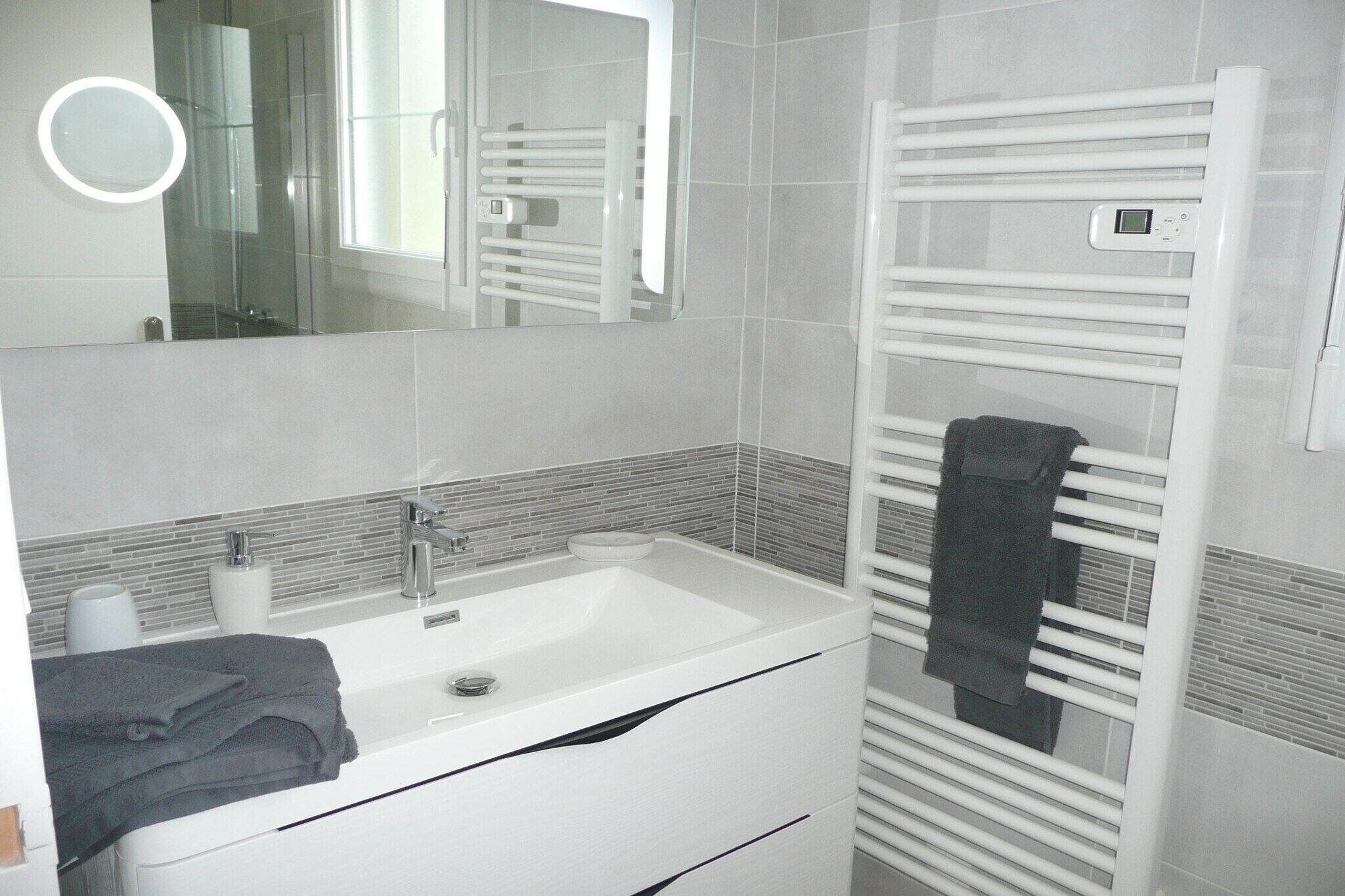 Une salle de bain moderne avec un lavabo blanc, un miroir et un porte-serviettes.