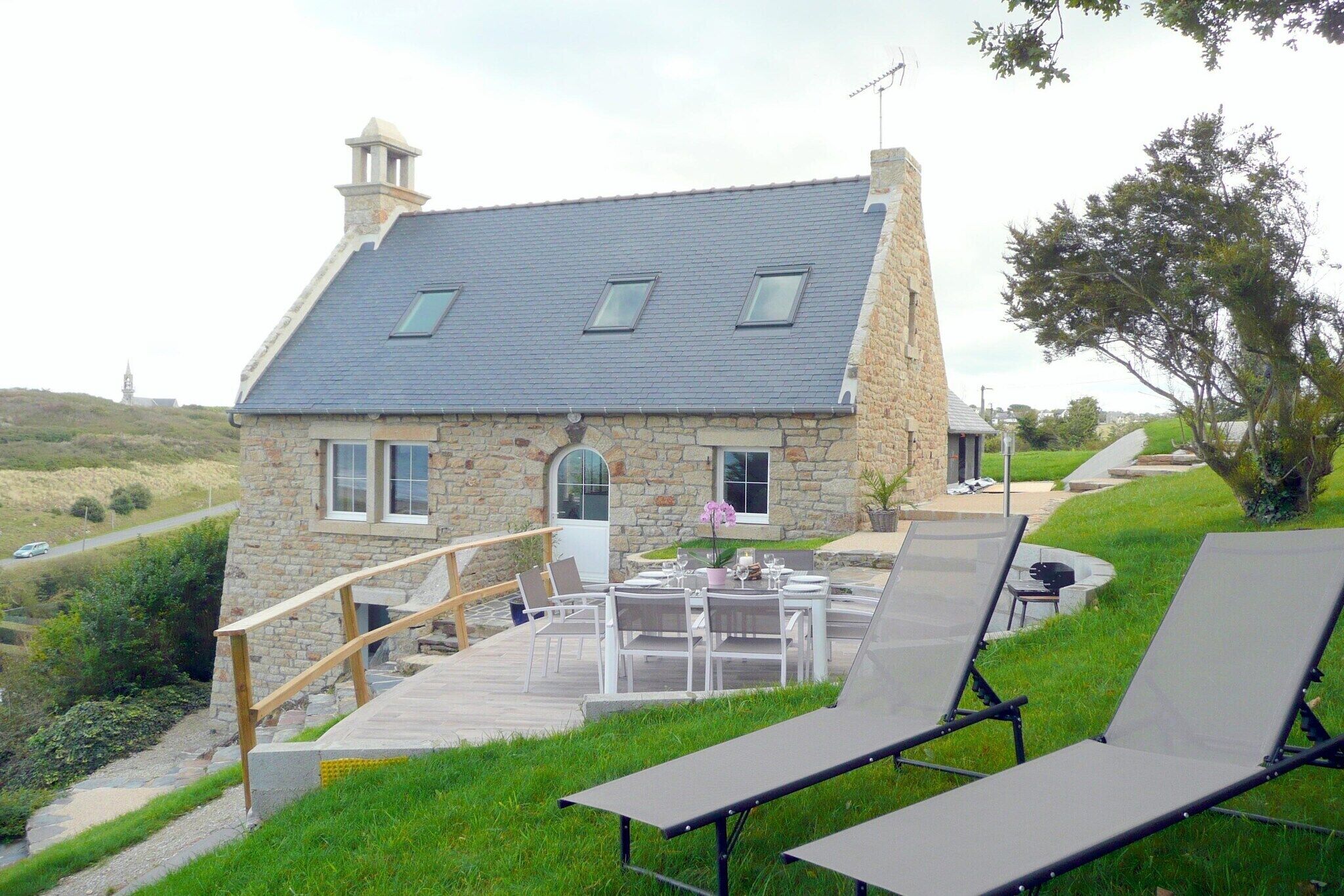 Una casa de piedra con techo inclinado, un patio con muebles de exterior y un paisaje cubierto de césped.