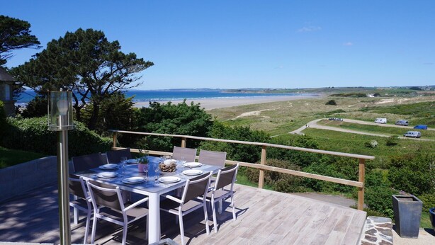 Une table à manger avec des chaises, installée sur une terrasse extérieure offrant une vue sur la plage et le paysage environnant.