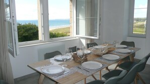 Un coin repas avec vue sur la mer, une table dressée pour quatre personnes et une cheminée.