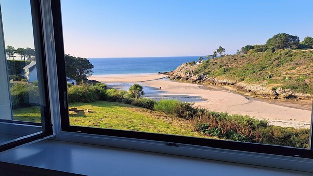 A coastal view through a window, including a beach, grassy area, and a hillside. - Spacious Coastal Villa near Rospico Beach (Nevez)
