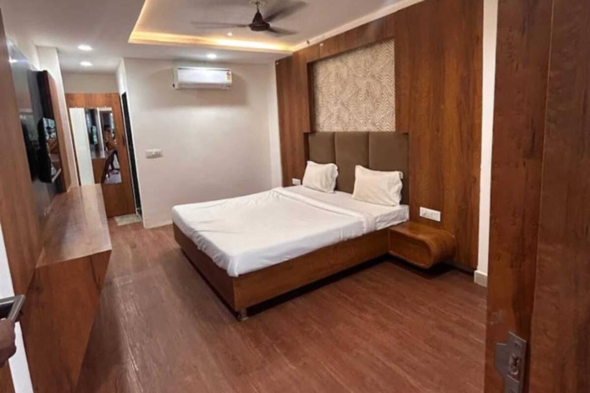 Un dormitorio moderno con piso de madera, cama con ropa de cama blanca, ventilador de techo e iluminación empotrada.