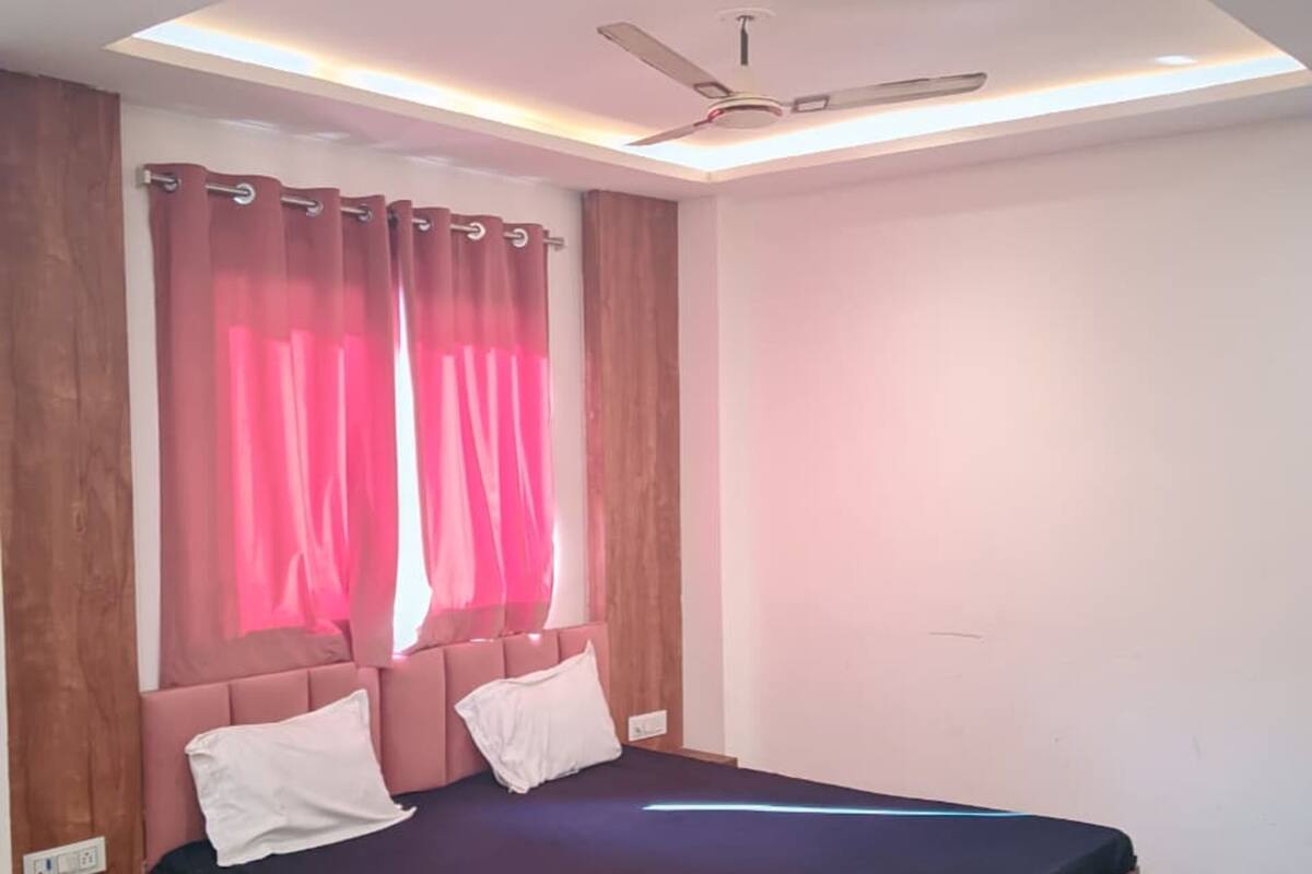 Un dormitorio con cama, cabecera de madera, ventilador de techo y cortinas rosas.
