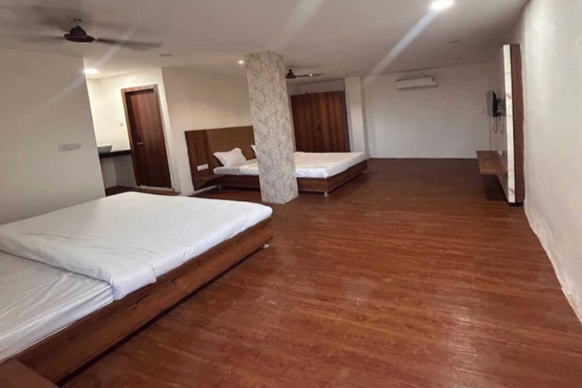 Habitación de hotel con dos camas, piso de madera, ventilador de techo y aire acondicionado de pared.