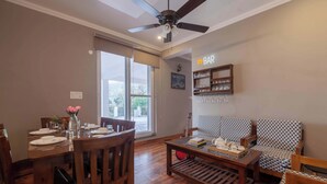 A dining area with a wooden table set for four, a sofa, and a ceiling fan. - Alaya Stays Amara Twilight (Naina Range)