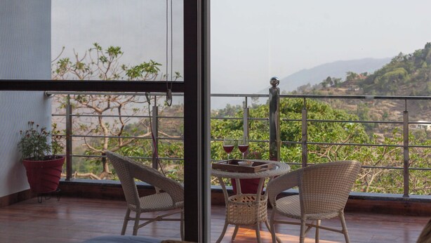 A balcony with wicker chairs, a small table with drinks, and a potted plant. - Alaya Stays Amara Twilight (Naina Range)