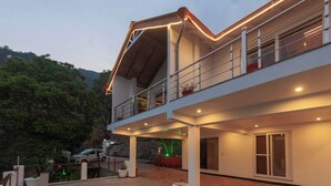 A modern two-story building with a balcony, potted plants, and a paved courtyard. - Alaya Stays Amara Twilight (Naina Range)