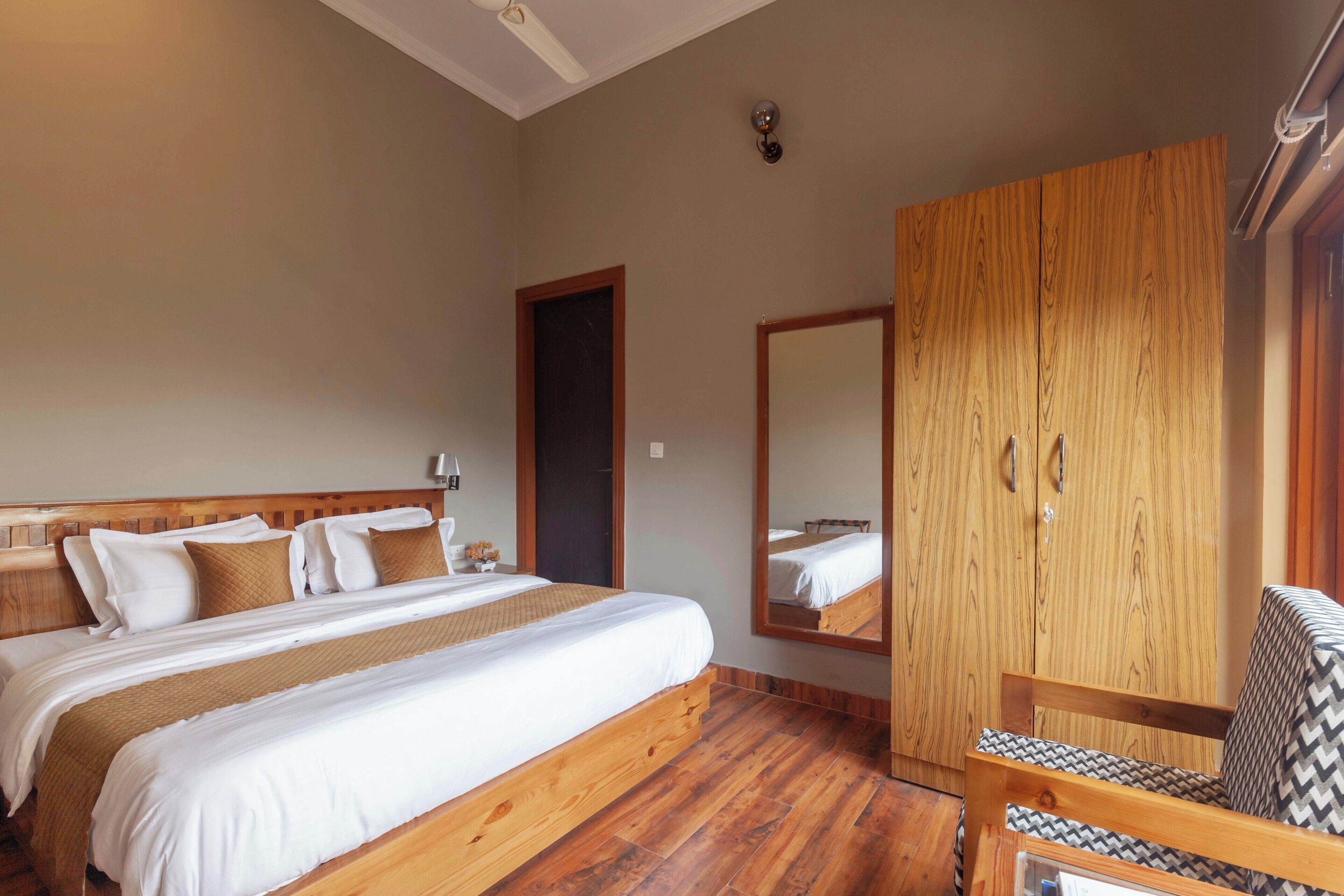 A hotel room with a large bed, a wooden wardrobe, and a chair.
