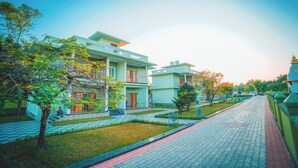 A modern building with multiple floors, a paved pathway, and trees. - Jai Ganesha Resort (Mal)
