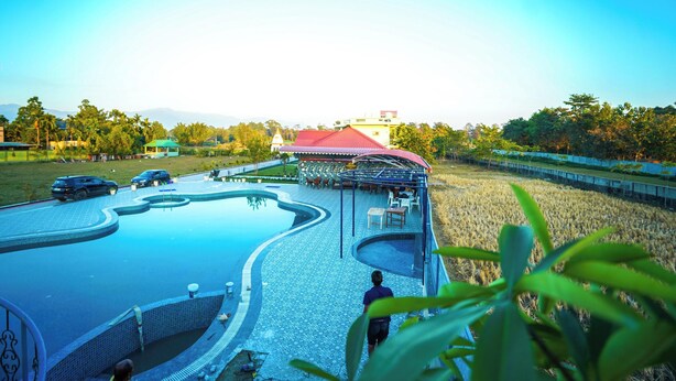 A swimming pool with a red-roofed pavilion, a grassy area, and a distant building. - Jai Ganesha Resort (Mal)