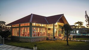 A two-story building with a checkered patio, a garden with potted plants, and a swimming pool in the background. - Jai Ganesha Resort (Mal)