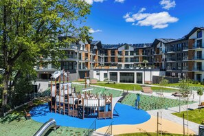 A playground with climbing structures and a slide, surrounded by modern apartment buildings with large windows and balconies. - Laguna Beskidów Resort & Spa (Zarzecze)
