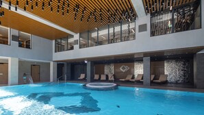 Ein Innenpool mit Whirlpool, Liegestühlen und einer Holzbalkendecke.