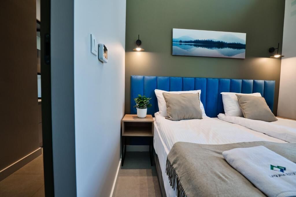 Ett hotellrum med en säng, ett nattduksbord med en växt, en tavla som hänger på väggen och en blå sänggavel.
