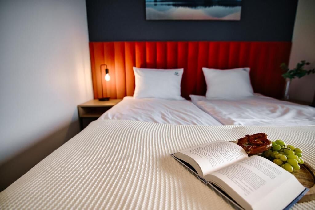 Een hotelkamer met een bed, een bedlampje, een boek, en een dienblad met druiven en gebak.