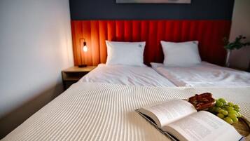 Een hotelkamer met een bed, een bedlampje, een boek, en een dienblad met druiven en gebak.
