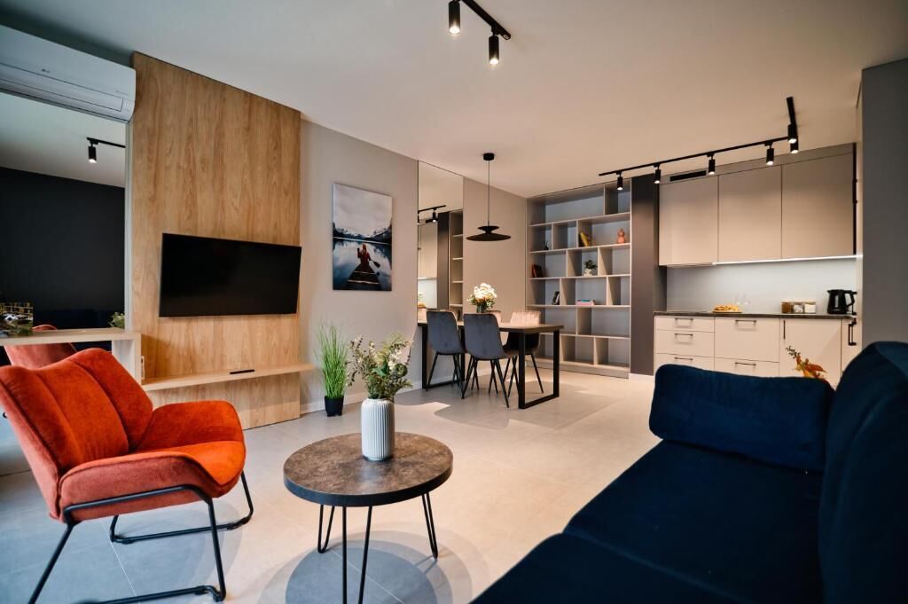 A modern living room with a sofa, armchair, TV, dining area, and kitchen.