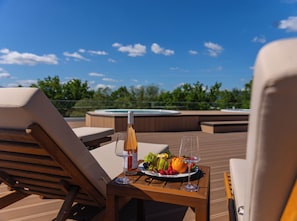 A wooden deck with lounge chairs, a hot tub, and a table with a fruit plate and wine glasses.