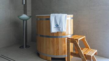 A wooden barrel-shaped sauna with a towel on top, a wooden stool, and a metal basin.