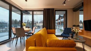 A modern living room with a sofa, chairs, a dining table, and a TV.