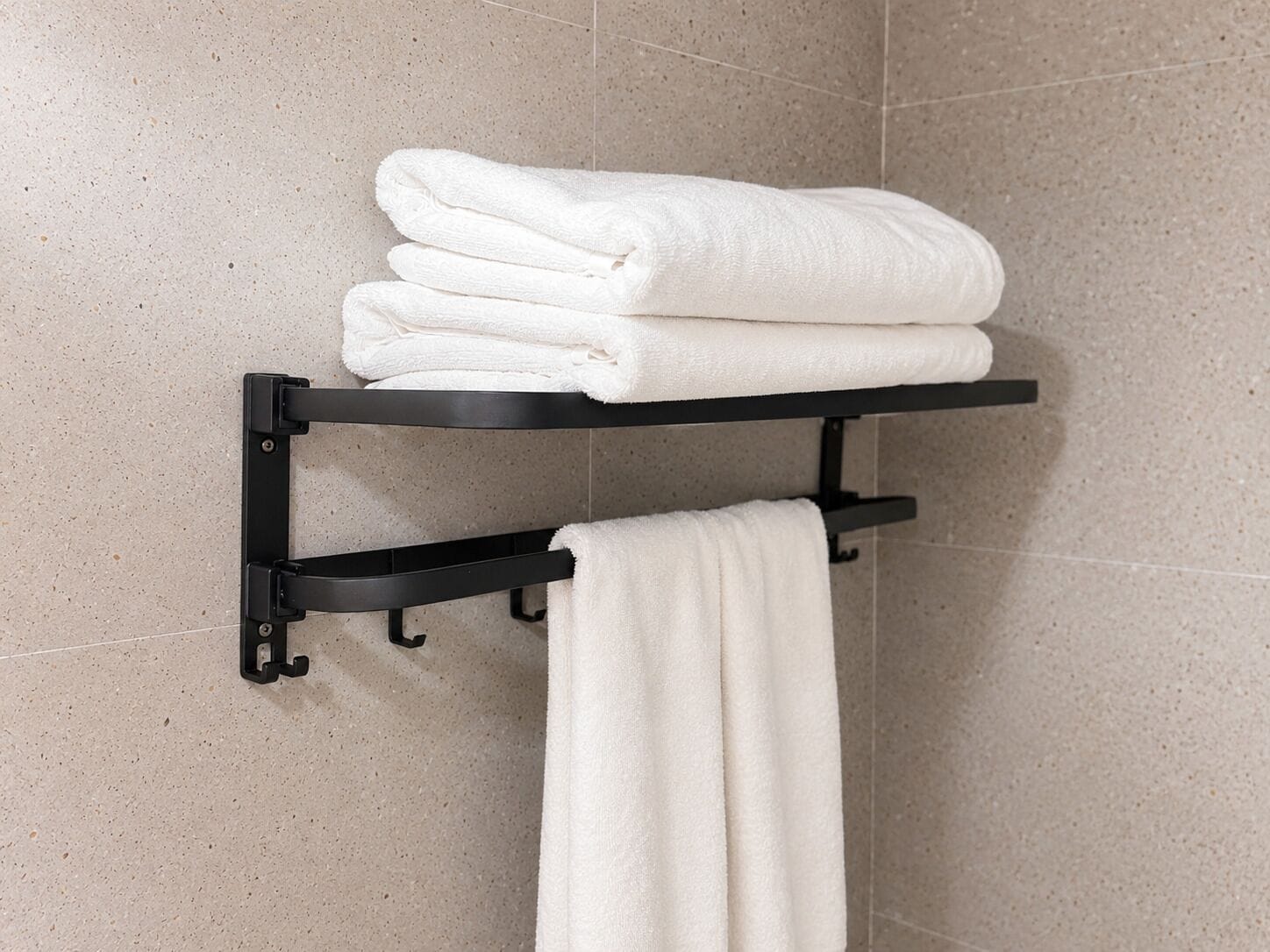 A bathroom with a towel rack holding folded towels and a single towel hanging.