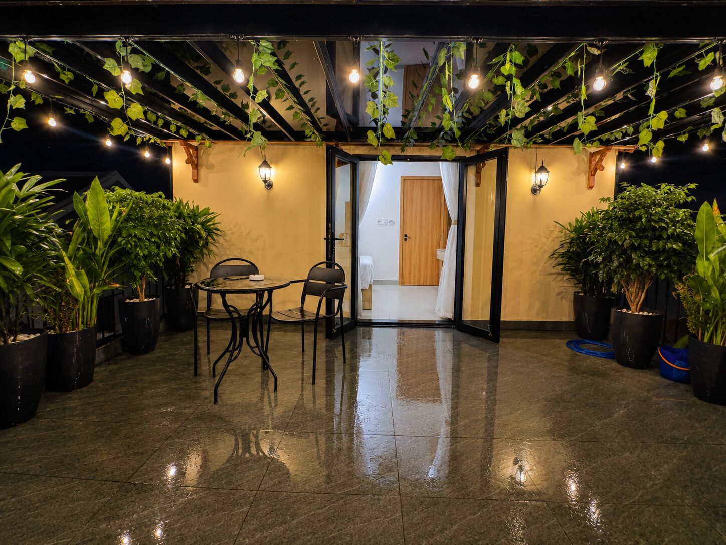 A wet floor in a lobby with a table and chairs, potted plants, and hanging vines.