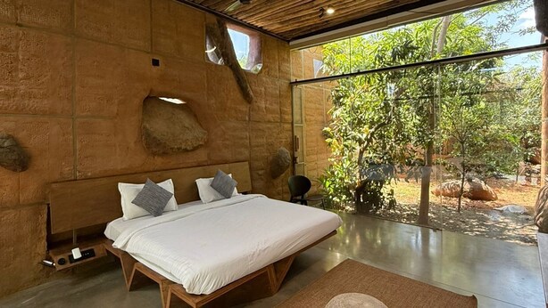 Une chambre moderne avec un plafond en bois, un grand lit, un mur en pierre et une vue sur la verdure.