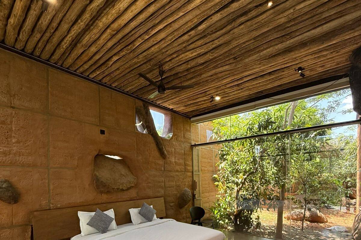 Un dormitorio moderno con techo de madera, una cama grande, pared de piedra y vistas a zonas verdes al exterior.