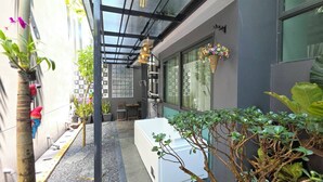 A narrow outdoor corridor with a white bench, potted plants, and a hanging flower basket. - A104- 1 Bedroom Serviced Apartment with Whirlpool at Ao Nang Beach (Tambon Ao Nang)