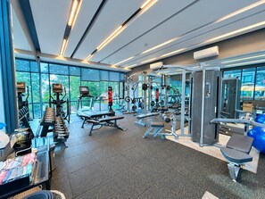 Ett modernt gym med olika typer av träningsutrustning, stora fönster och utsikt över grönområden utanför.
