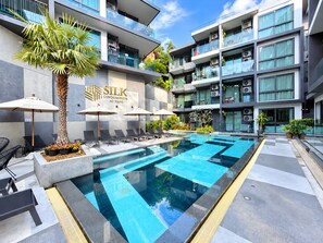 En modern byggnad med en swimmingpool, solstolar och parasoller.