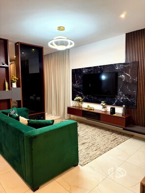 Un salon moderne avec un canapé vert, un téléviseur à écran plat et un mur décoratif en marbre.