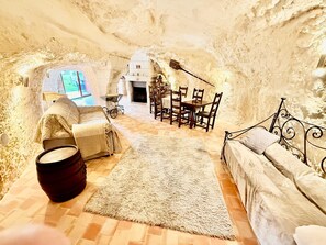 Ein unterirdischer Raum mit Kamin, einem Esstisch mit Stühlen, einer Couch und einem Teppich.